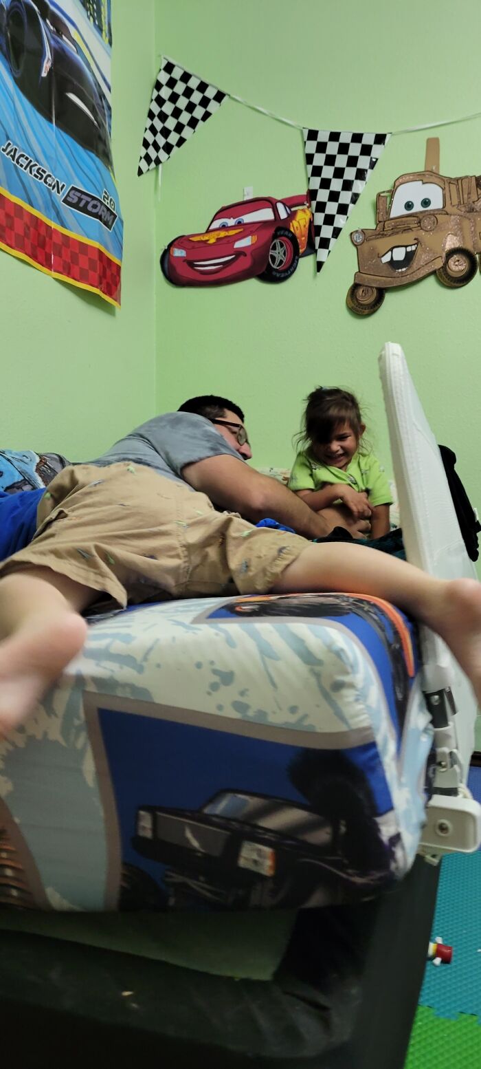 A man lying on a bed with a child, creating a strange angle that needs a second look to understand.