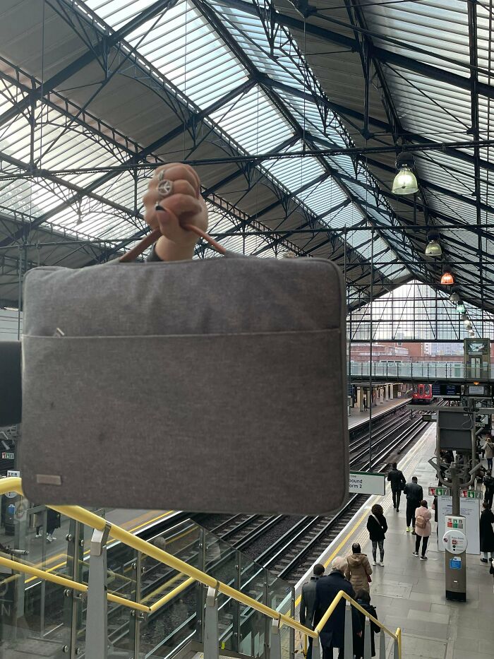 A person holding a grey bag at a train station, creating a visual trick that needs a second look.