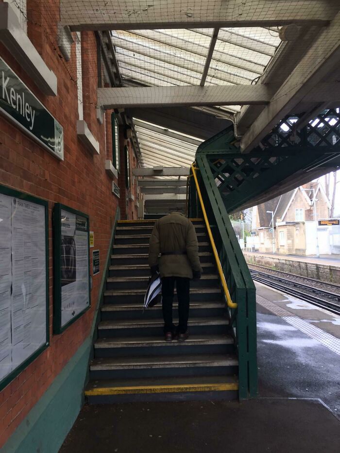 A person without a visible head walking up stairs at a train station, an image you may need to look twice at.