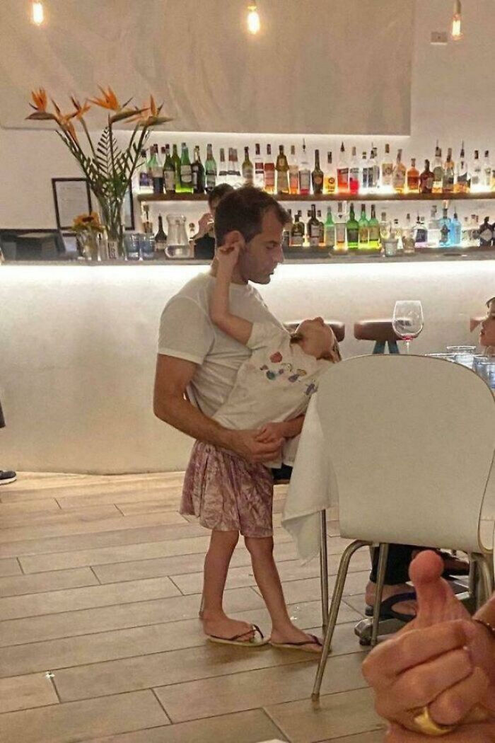A man holding a small child, an optical illusion making it seem like the child has adult legs, needing a second look.