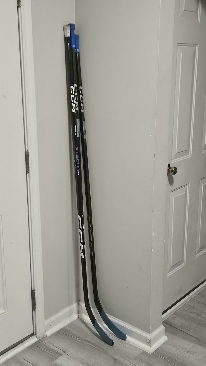 Several hockey sticks leaning against a wall next to a door, a photo you may need to look twice at.