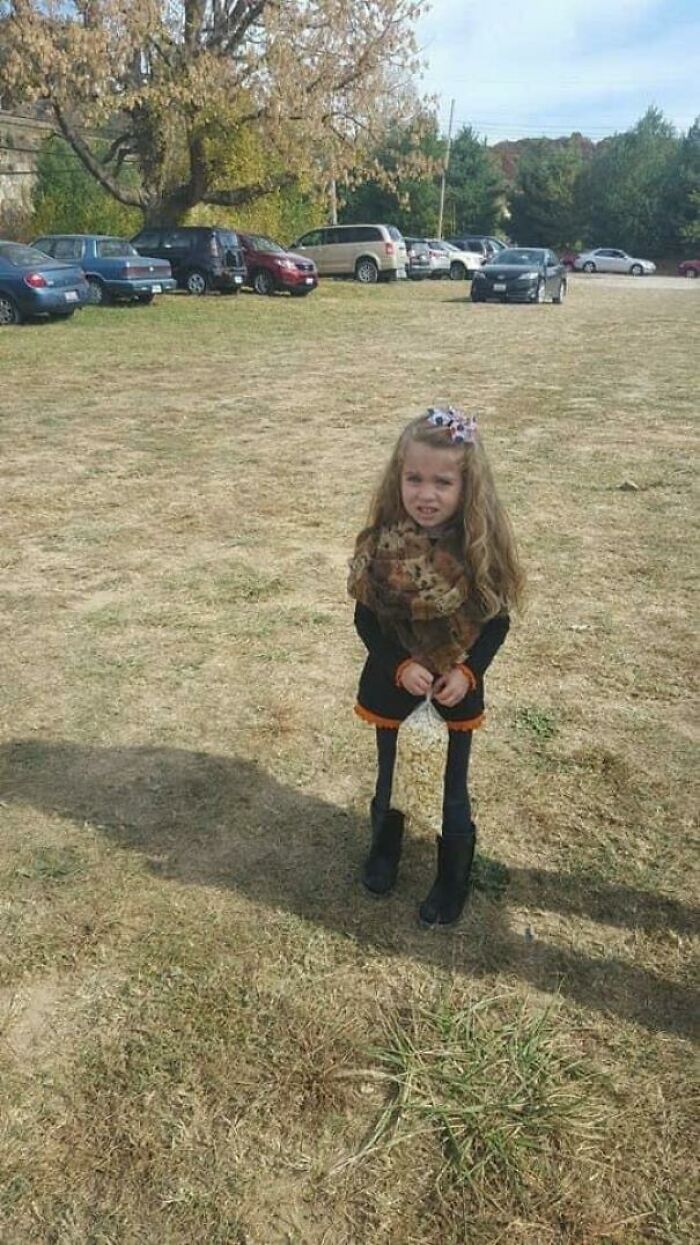 A young girl in a field, with a perspective that makes her legs appear disproportionately long, making you look twice to understand.