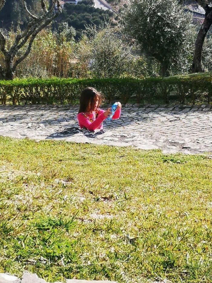 A girl appears to be half-buried in a paved path, a tricky photo that makes you look twice to understand.
