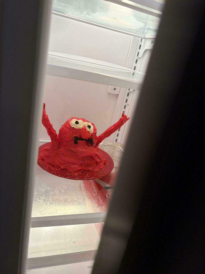 An amazing baker's red monster cake with white eyes and black mouth, sitting on a clear plate inside a refrigerator.