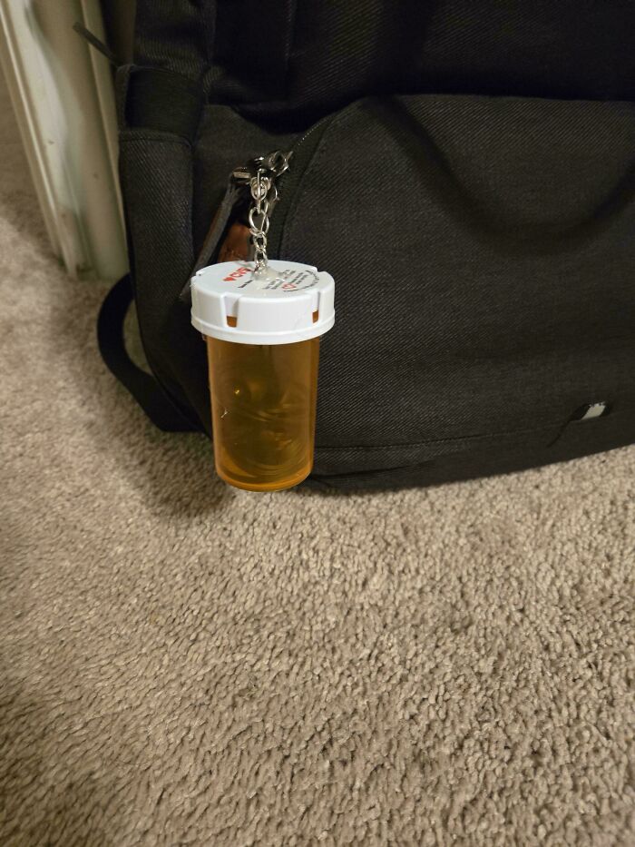 An orange pill bottle keychain attached to a black backpack, demonstrating creativity in reusing old junk.