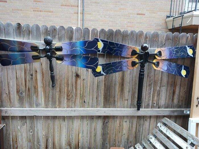 Two decorative dragonflies, creatively made from old junk ceiling fan blades, hanging on a wooden fence.