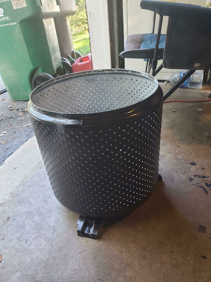 A large washing machine drum repurposed from old junk, ready for creative transformation in a garage.