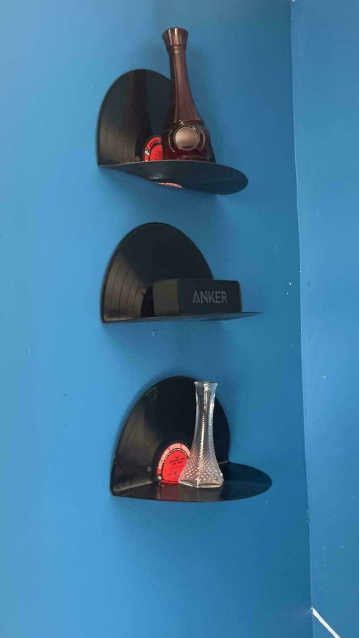 Three shelves made from old junk, vinyl records, displaying small decorative items on a blue wall.