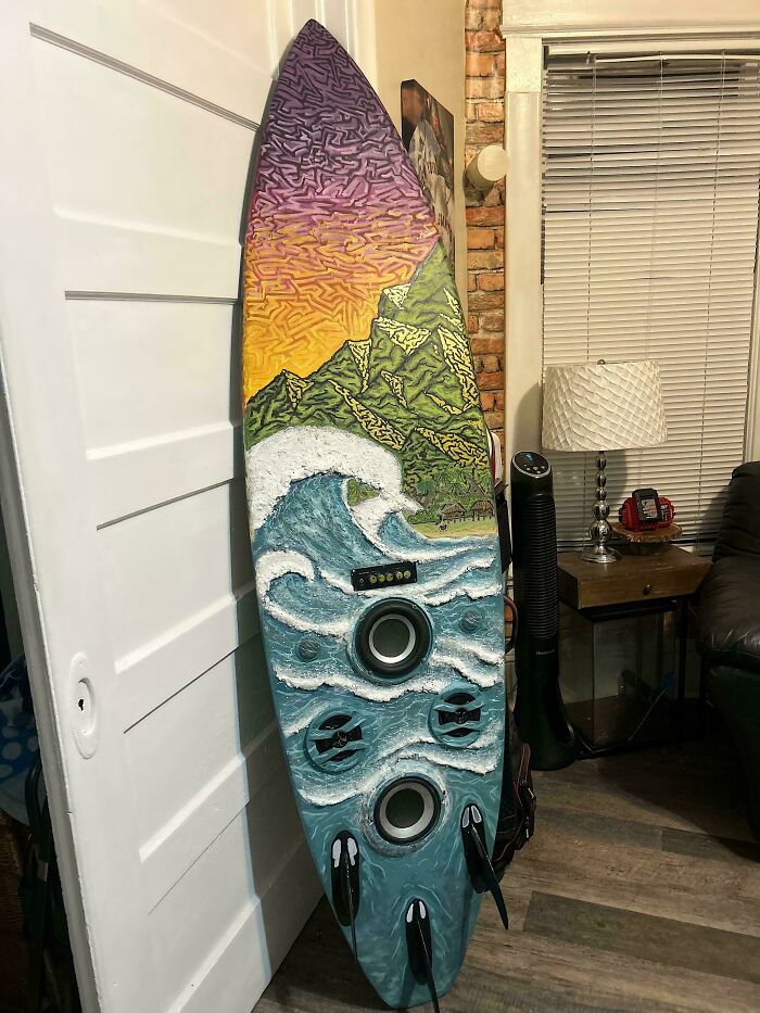 An old junk surfboard repurposed into art, depicting a vibrant ocean scene with speakers integrated.