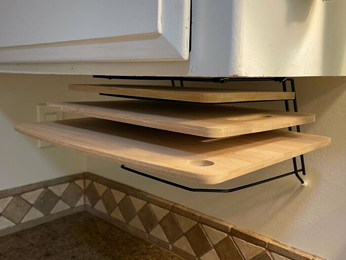 Cutting boards stored neatly on an under-cabinet rack, a creative solution for organizing kitchen junk.