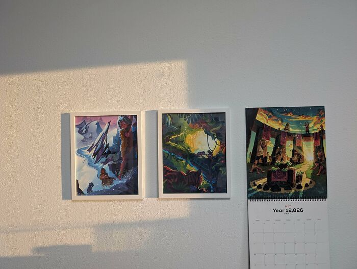 Three pieces of art and a calendar on a white wall, showcasing creativity.