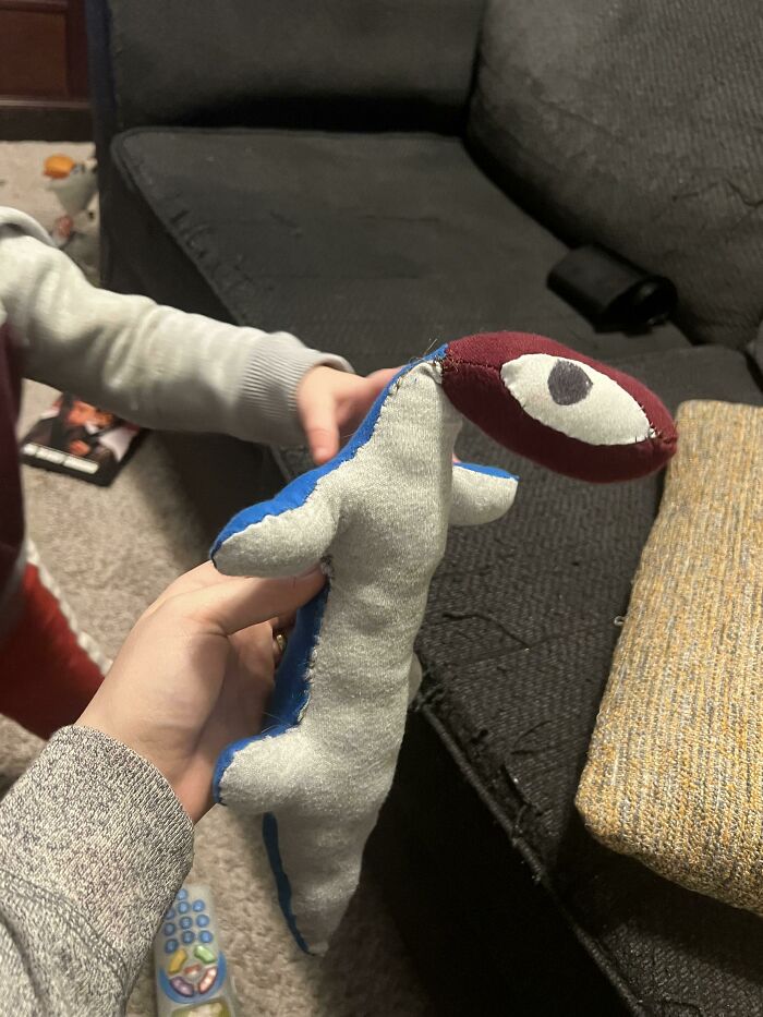 A handmade dinosaur plush toy, made from old junk, held in a child's hands, showcasing creativity.