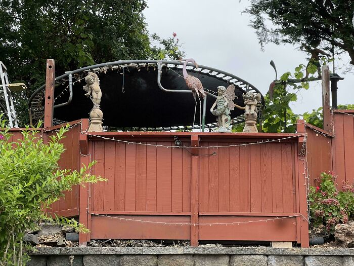 A backyard scene featuring various old junk items creatively repurposed, including a trampoline and garden statues.