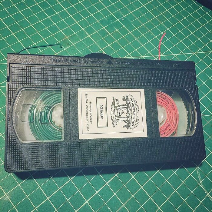 A creative way to reuse old junk: a VHS cassette tape with green and red spools on a green grid mat.