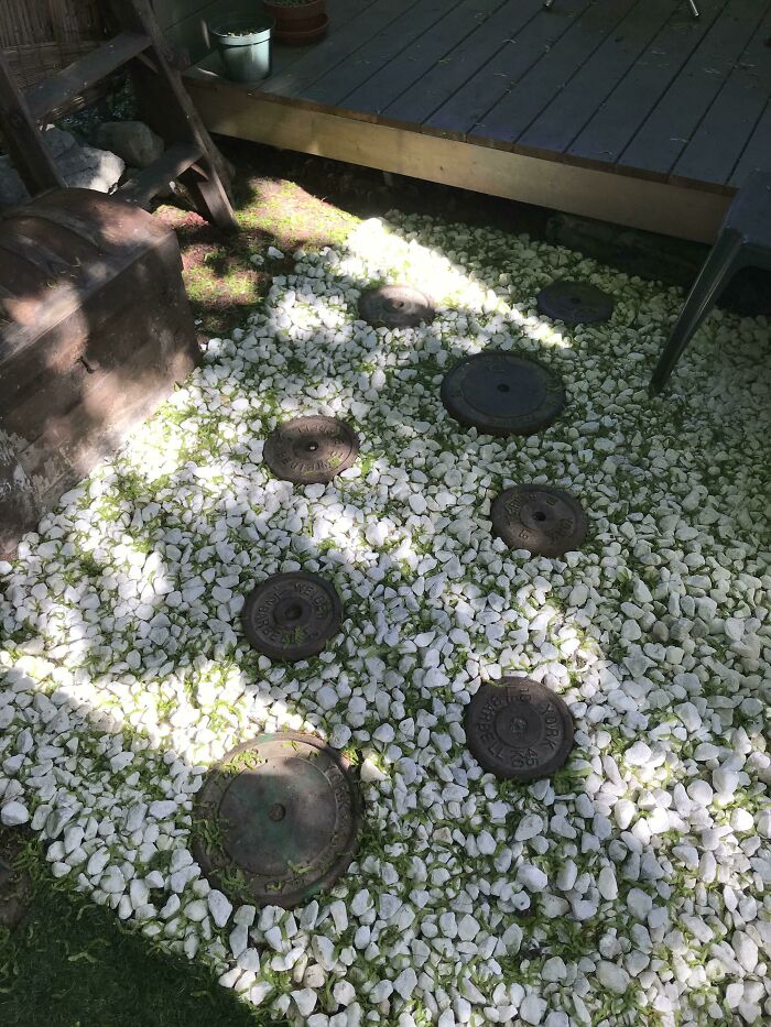 Garden path featuring round, rusted metal weights on white pebbles, demonstrating how old junk can be creatively reused.