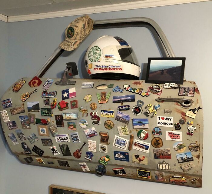 An old junk car door repurposed as a display for travel stickers and a helmet, showing creativity.