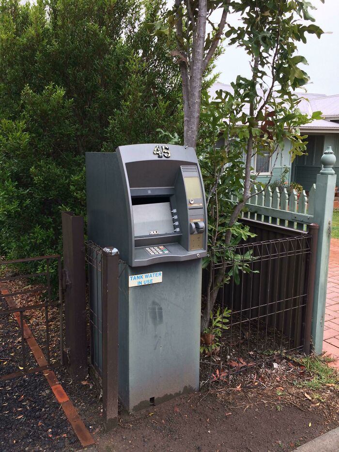 An outdoor ATM next to a gate and trees, representing old junk possibly repurposed for a new use.