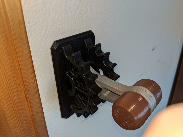 A unique 3D printing creation, a functional gear mechanism mounted on a wall, with a small hammer attached.