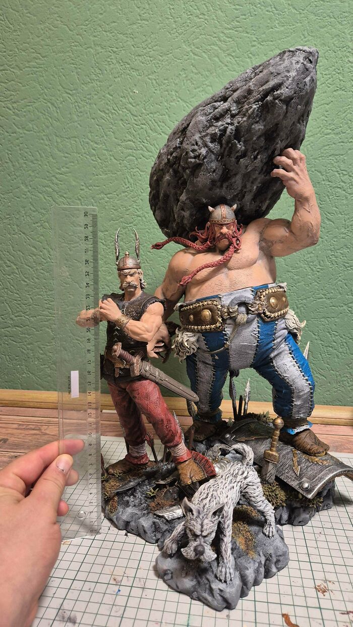Two large, highly detailed 3D printing creations of comic book characters, one holding a rock, next to a ruler.
