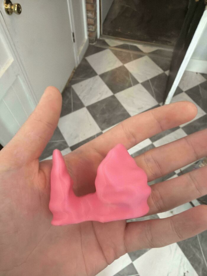A hand holding a small, pink, organically shaped 3D printing creation, showing off an amazing creation.