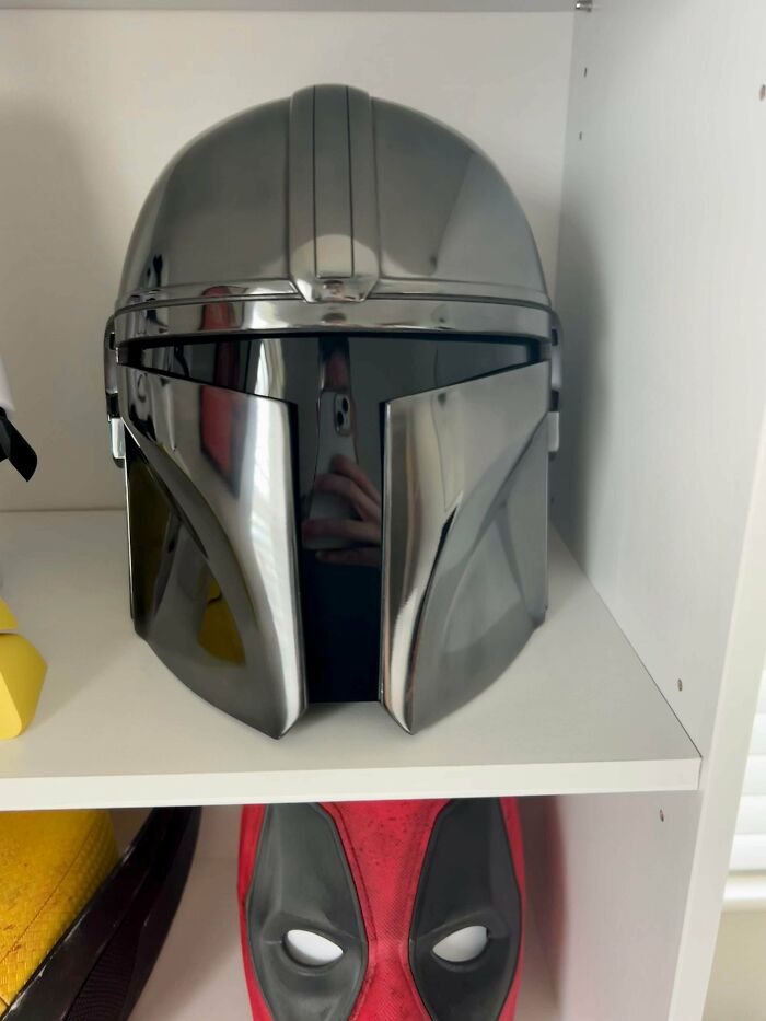A shiny, metallic grey 3D printing Mandalorian helmet displayed on a white shelf, an amazing creation.