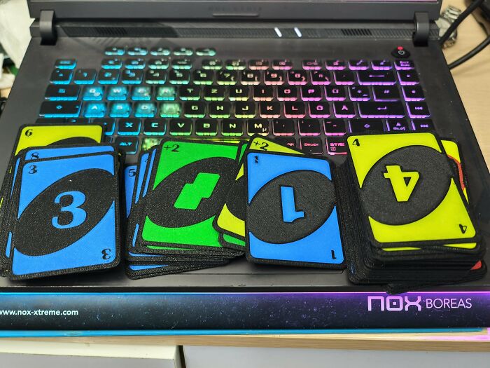 Amazing 3D printing creations: custom UNO cards with numbers and symbols on a laptop with a lit keyboard.