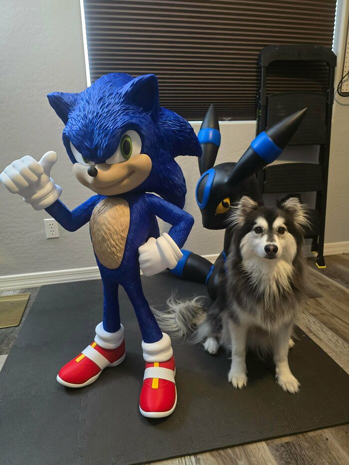 A loyal dog sits beside two amazing 3D printing creations: a large Sonic the Hedgehog and a dark Pokemon character.