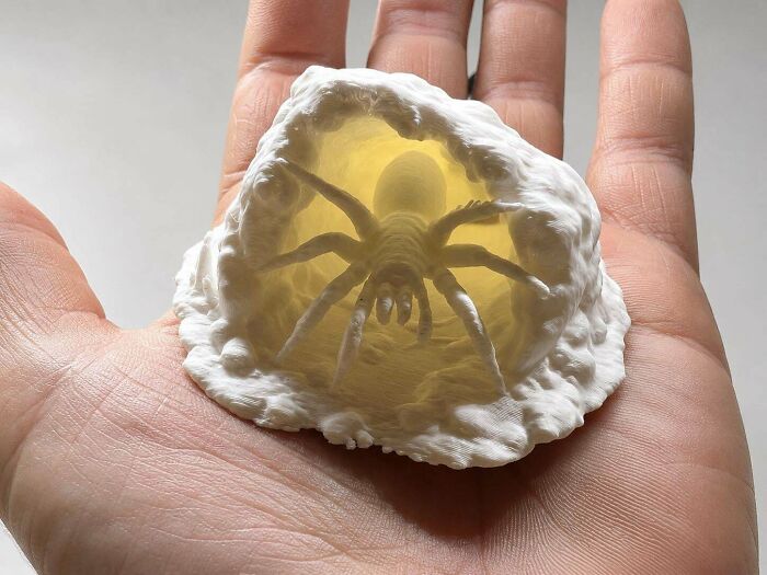 Amazing 3D printing creation of a glowing spider in its web held in a person's hand.