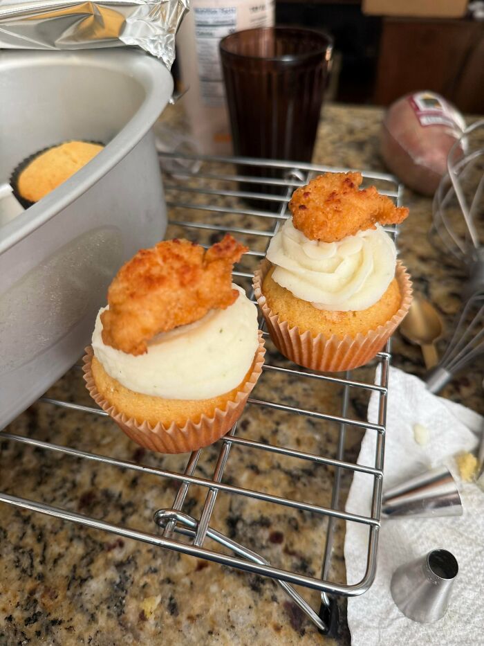 Delicious cupcakes by a baker, topped with white frosting and crispy fried chicken pieces for an amazing treat.