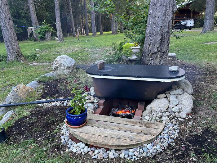 An old bathtub repurposed as an outdoor hot tub with a fire pit underneath, a clever solution.