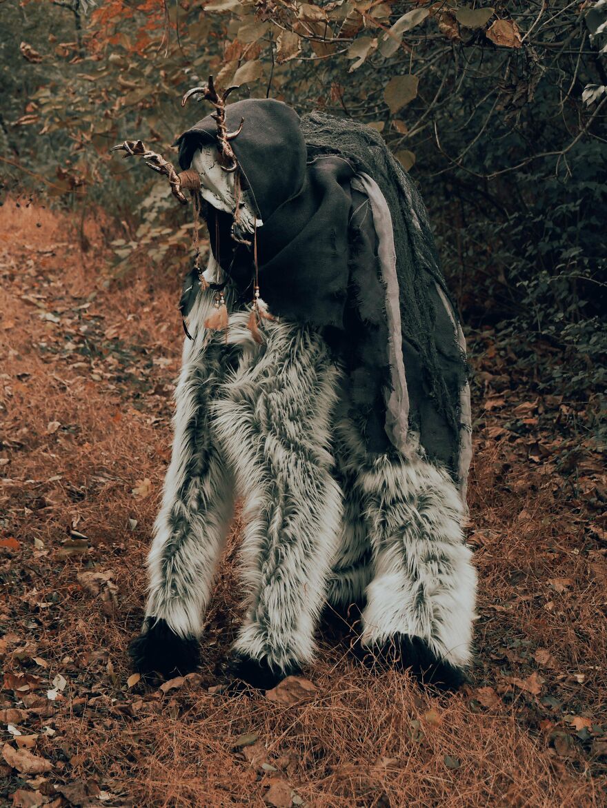 A person in a whimsical crafts deer-like costume with antlers and fur, standing in a forest setting.