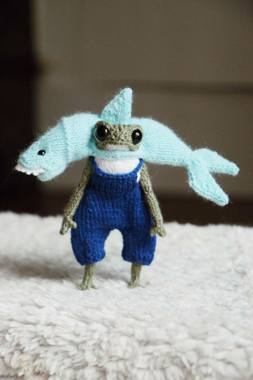 A knitted frog wearing blue overalls and a blue shark hat, showcasing magical whimsical crafts.