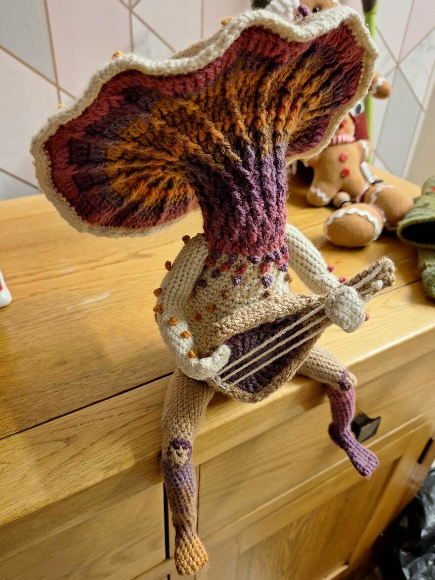 A whimsical craft of a crocheted mushroom creature with a large, colorful cap, holding a small string instrument.