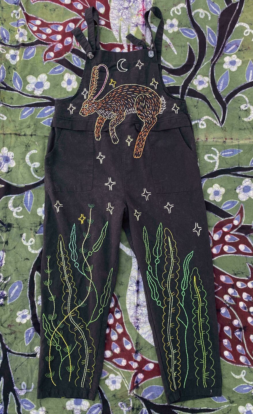 Black overalls featuring a whimsical craft of an embroidered rabbit and stars, with green seaweed-like designs on the legs.