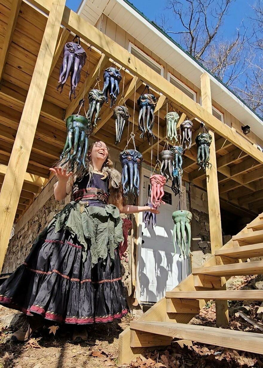 A person in a whimsical, magical craft outfit, surrounded by hanging colorful octopus sculptures under a deck.