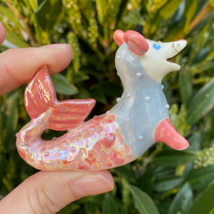 A hand holding a small, whimsical craft figurine of a mermaid-mouse with a pink tail and blue body.