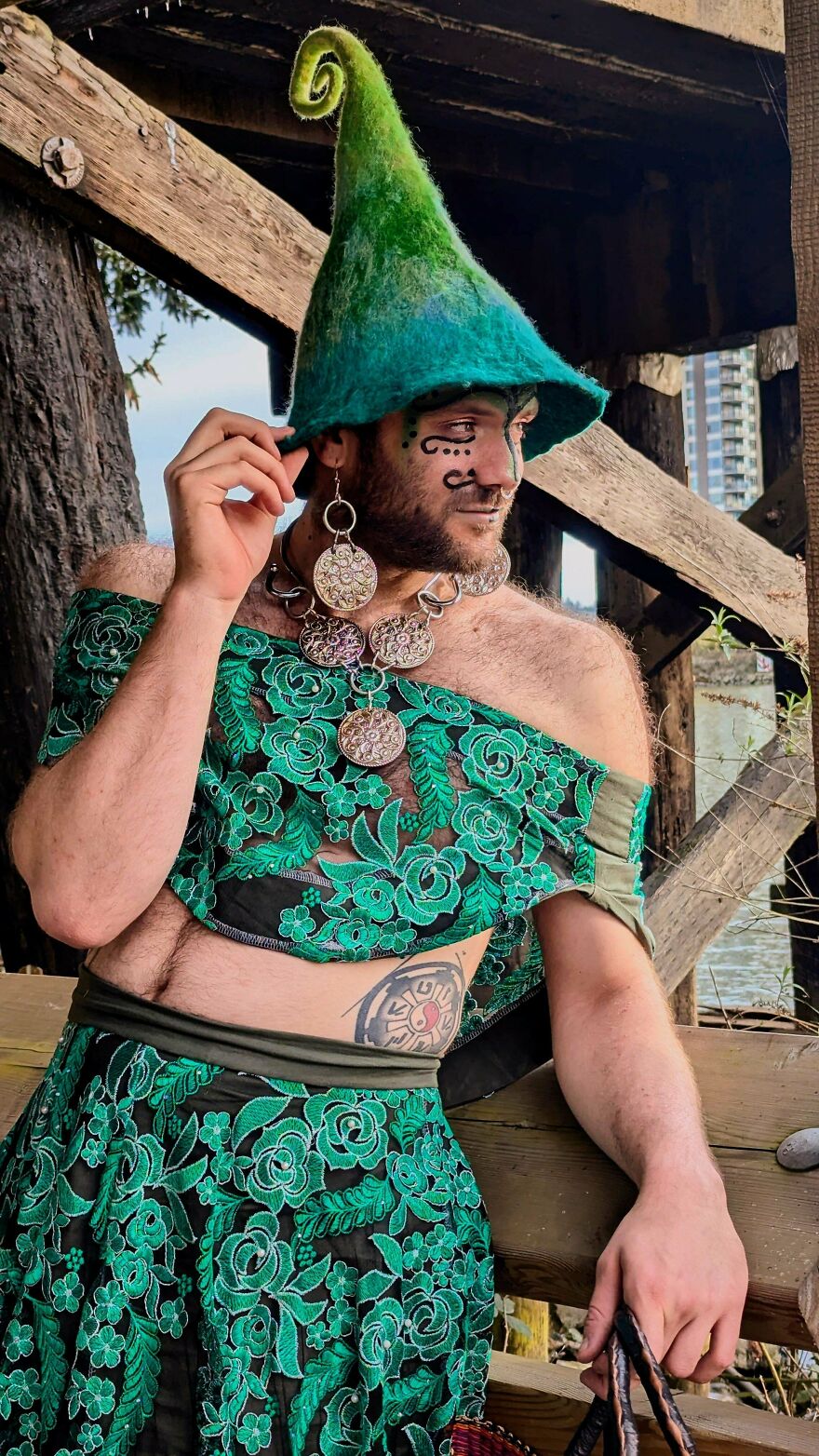 A person wearing a whimsical, magical craft outfit, including a green pointy hat, elaborate jewelry, and green lace clothing.