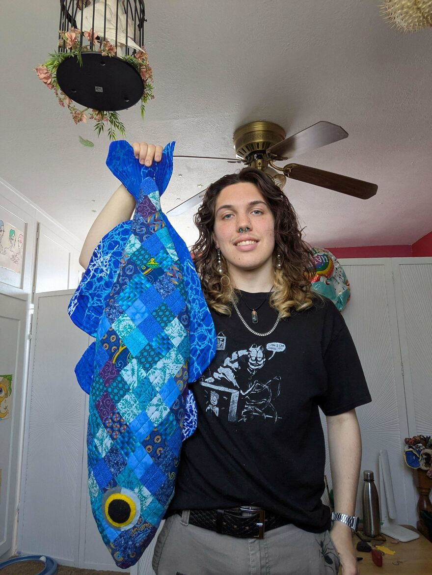 A person holding up a large, whimsical craft fish plushie made from various blue fabric patches.