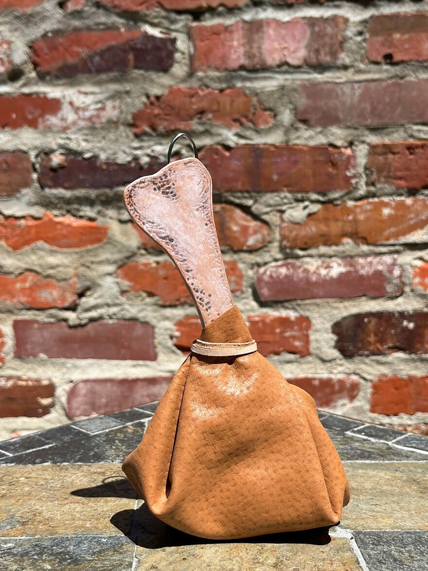 A quirky, brown, pouch-like whimsical craft with a bone-shaped handle, magical and shared online.