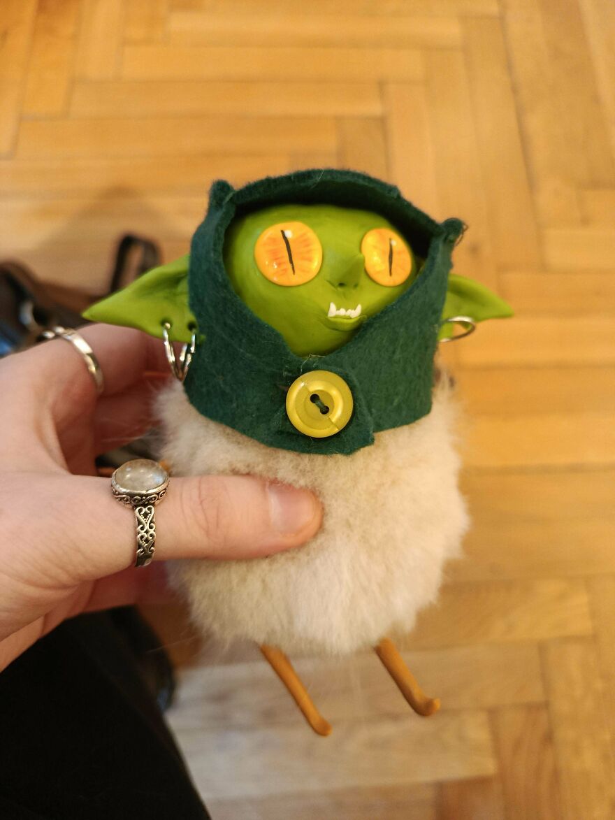 A person holding a cute, green-faced whimsical craft with a fuzzy body, magical and shared online.