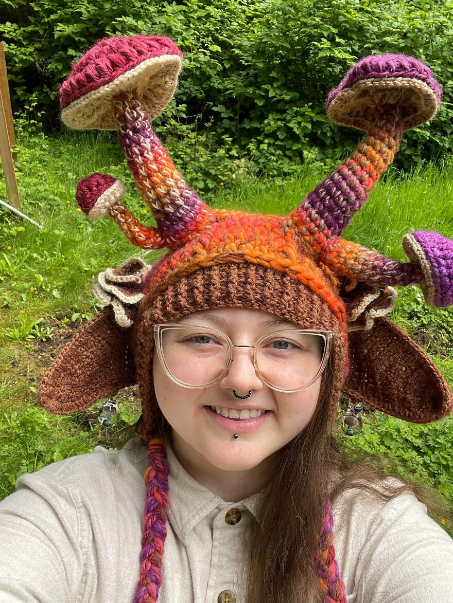 A woman smiling in a whimsical crafts mushroom hat, showcasing magical craftsmanship shared online.