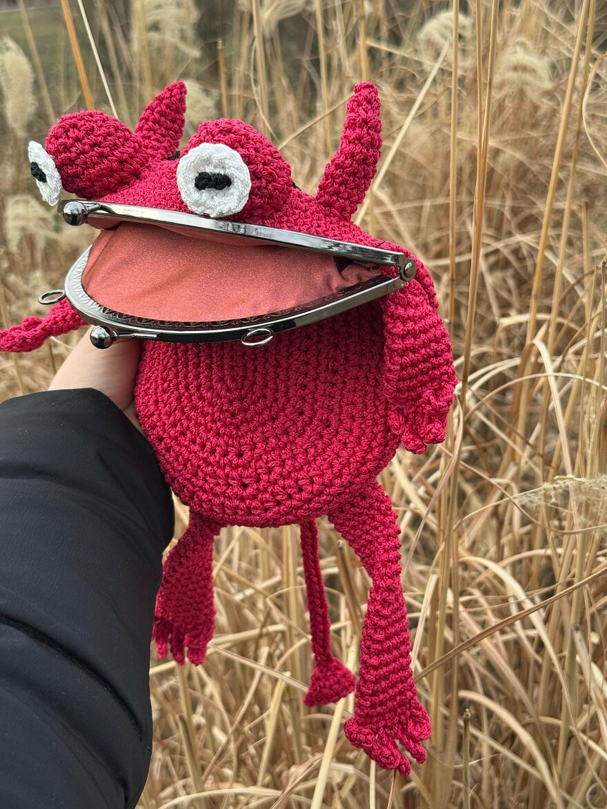 A person holding a whimsical, red crocheted monster with a wide-open mouth, a magical craft.