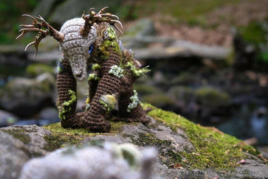 A close-up of a crocheted creature with branch-like antlers, a magical whimsical craft, on a mossy rock.