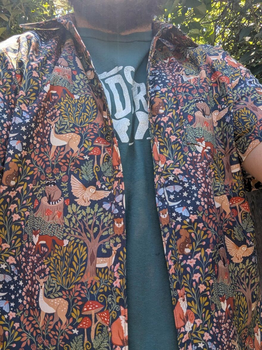 A person wearing a dark blue shirt adorned with a whimsical nature pattern featuring deer, foxes, and mushrooms.