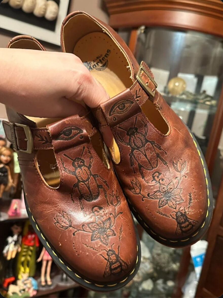 A pair of whimsical crafts brown leather shoes with intricate beetle and eye designs, featuring buckles and yellow stitching.