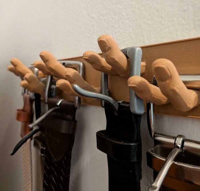 A 3D printer project featuring unique hand-shaped hooks holding various belts on a wooden strip.