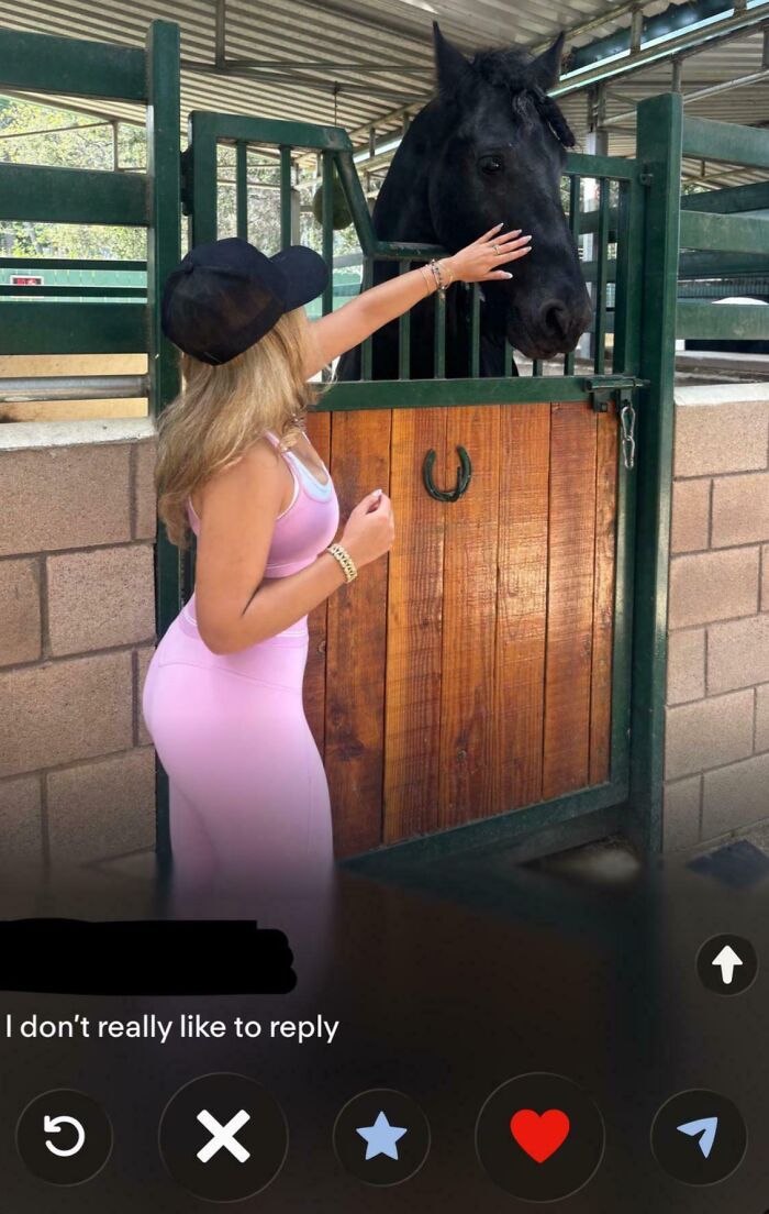 A woman in pink activewear petting a black horse in its stall, showcasing a cringe Tinder profile.