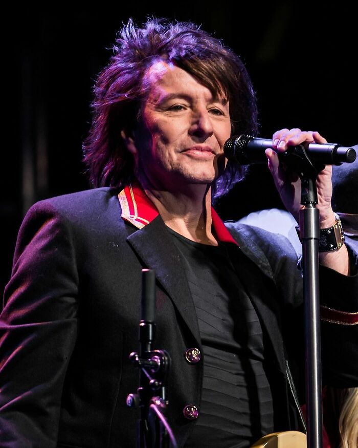 Richie Sambora performing live, holding a microphone. Image shows Richie Sambora's career highlights and bio.