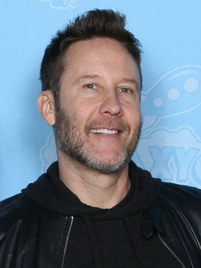 A headshot of actor Michael Rosenbaum with a beard, smiling at the camera, highlighting his career.