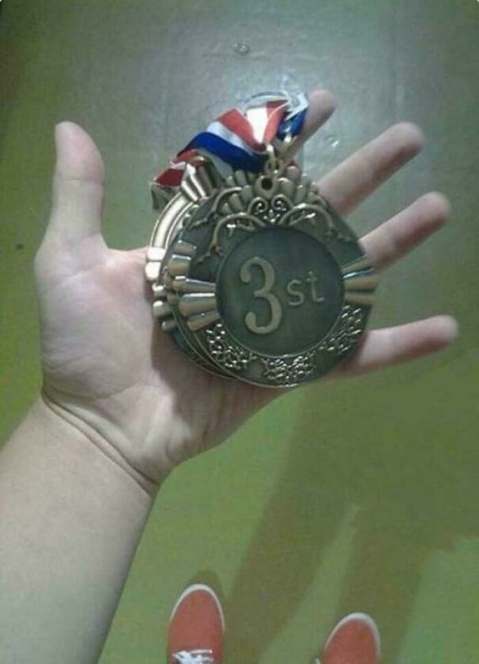 Funny 'You Had One Job' Fails: A hand holding a medal that reads 3st instead of 3rd, a funny sports award fail.